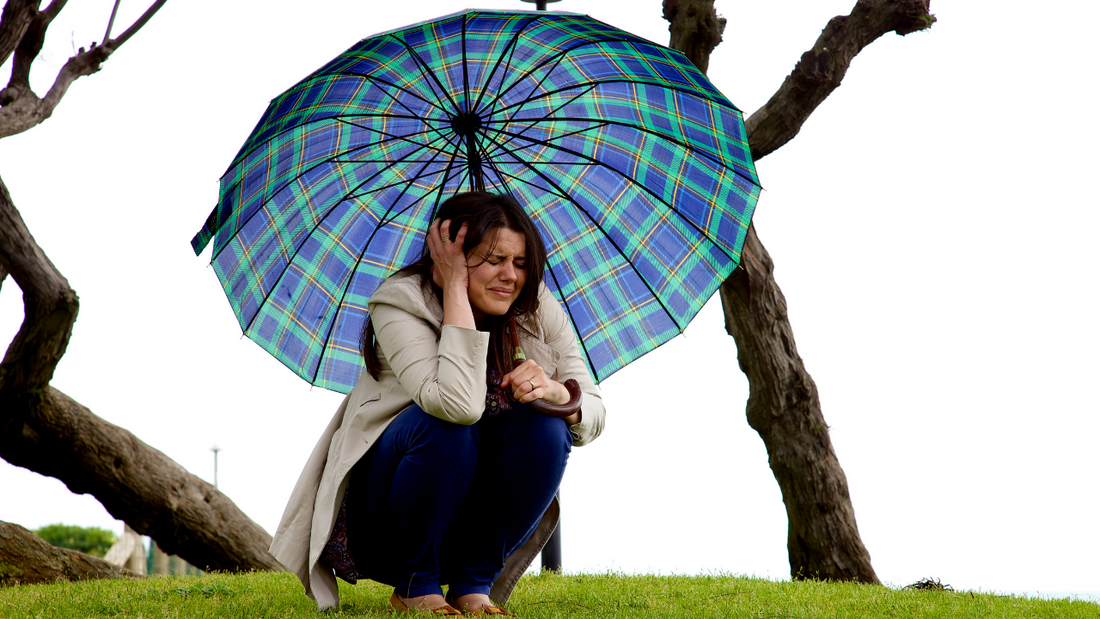 A woman crouches beneath an umbrella, preparing for a natural disaster.