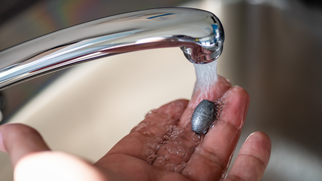 A person holding a metal pellet runs water over their fingers